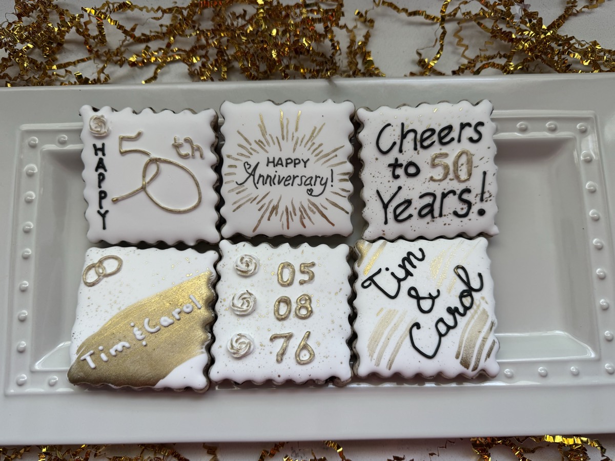 A gold and white 50th wedding anniversary decorated sugar cookie set reading "Happy Anniversary" and "Cheers to 50 Years!"