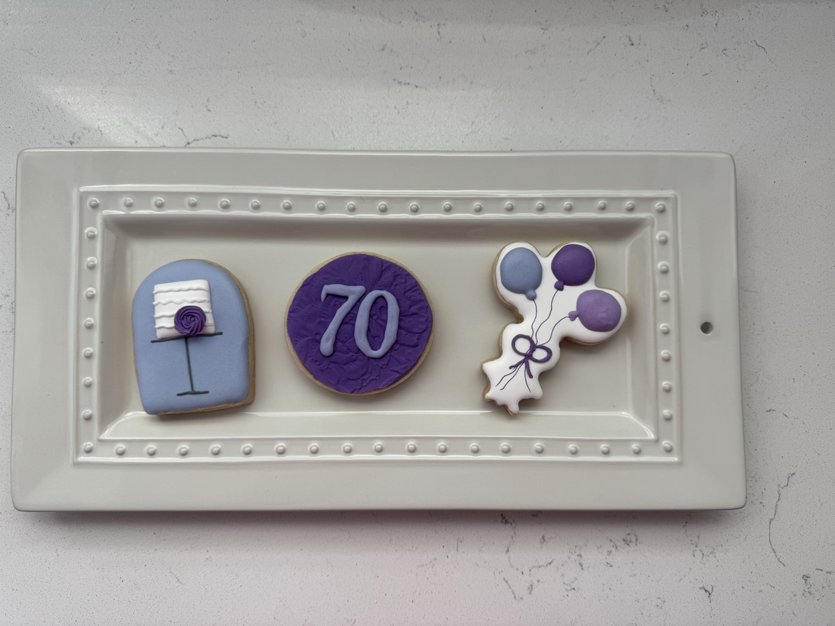 70th birthday decorated sugar cookies in purple and blue: a wrapped gift, a number 70 cookie, and a bunch of balloons