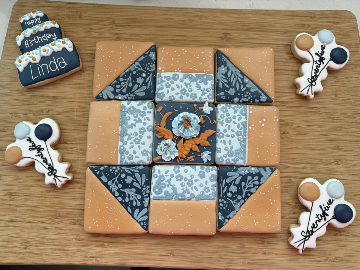 A quilt-patterned 75th birthday decorated sugar cookie platter in orange, navy, and floral prints, with matching name cookies