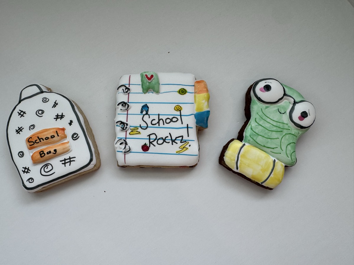 Back-to-school decorated sugar cookies shaped like a composition notebook reading "School Rocks", a name tag reading "School Boy", and a smiling frog