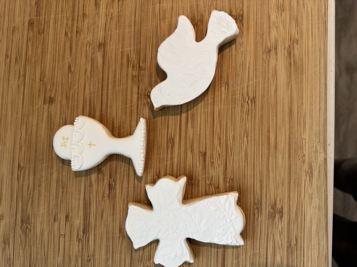 First Communion themed decorated sugar cookies: a lace cross, a chalice with a small gold cross, and a dove, in white and gold