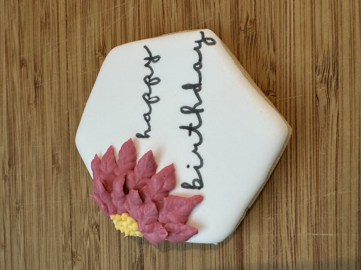 A white hexagon decorated sugar cookie with a pink floral spray and "happy birthday" script