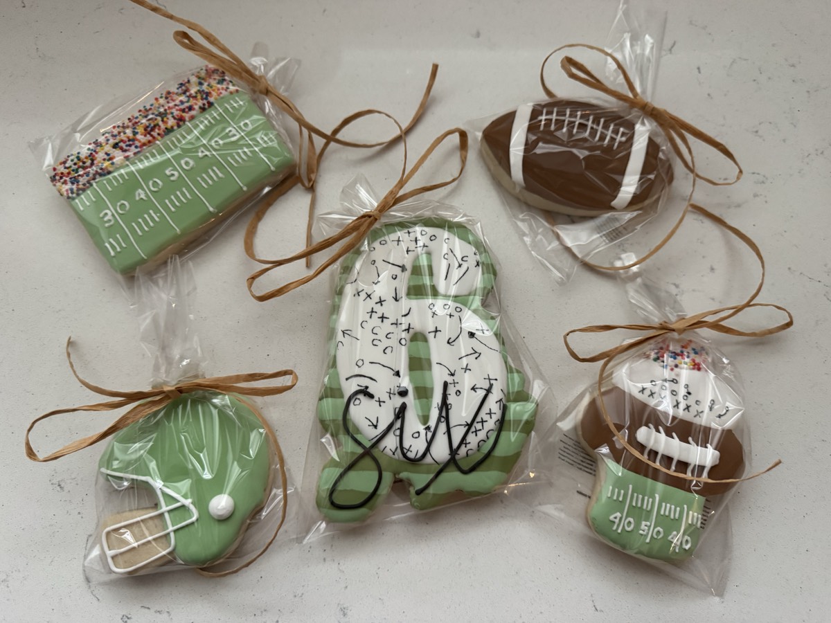 Individually wrapped football themed decorated sugar cookies: a green jersey, a sprinkle-topped cookie, a football field with plays drawn on it, a mini jersey, and a football