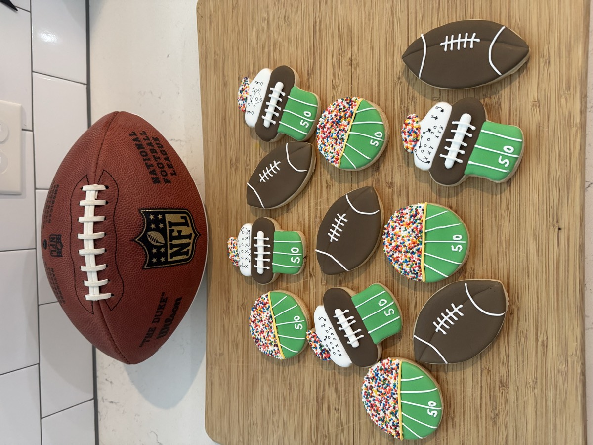 Football-themed decorated sugar cookies with football laces, striped end-zone cups, and yard-line lettering, styled with a real NFL football