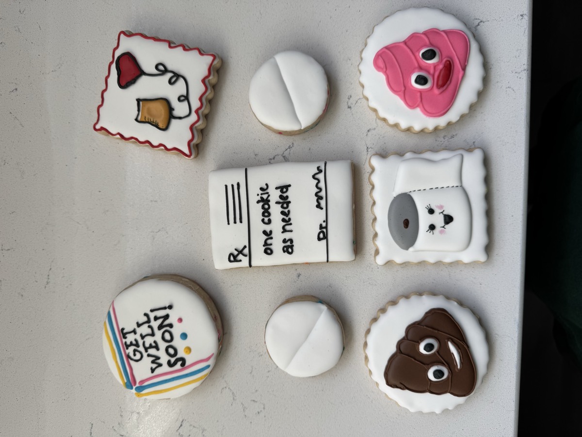 A humorous get-well decorated sugar cookie set with "Get Well Soon!", a prescription pad, pills, a toilet paper roll, and smiling cartoon cookies