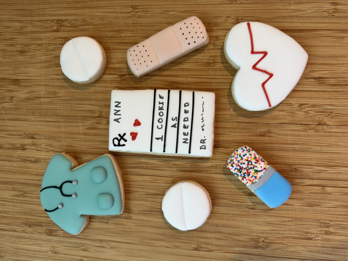 Medical-themed decorated sugar cookies: a pill, a bandage, an EKG heartbeat heart, a nurse scrub top, and a prescription pad reading "one cookie as needed"