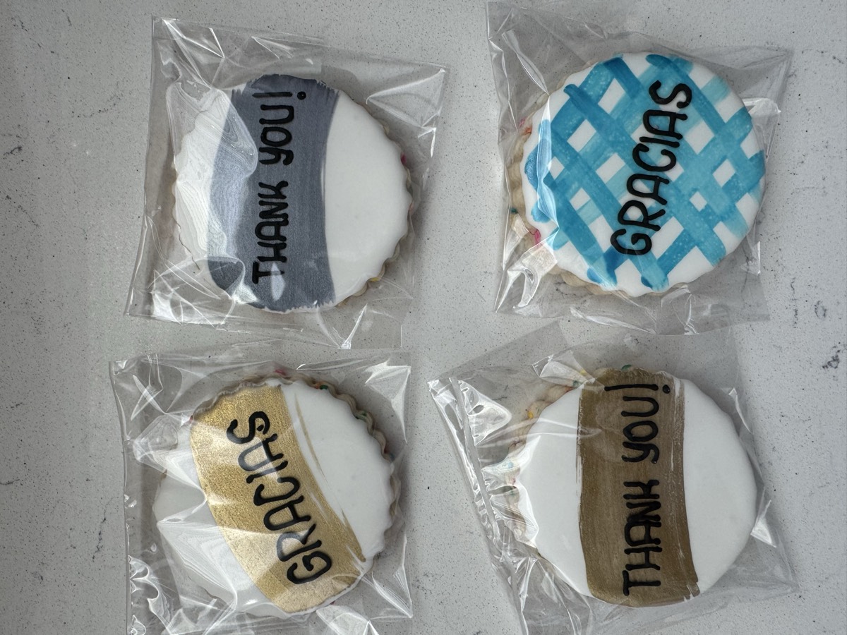 Round decorated sugar cookies reading "Gracias" and "Thank You!" in gold, gray, and blue lettering