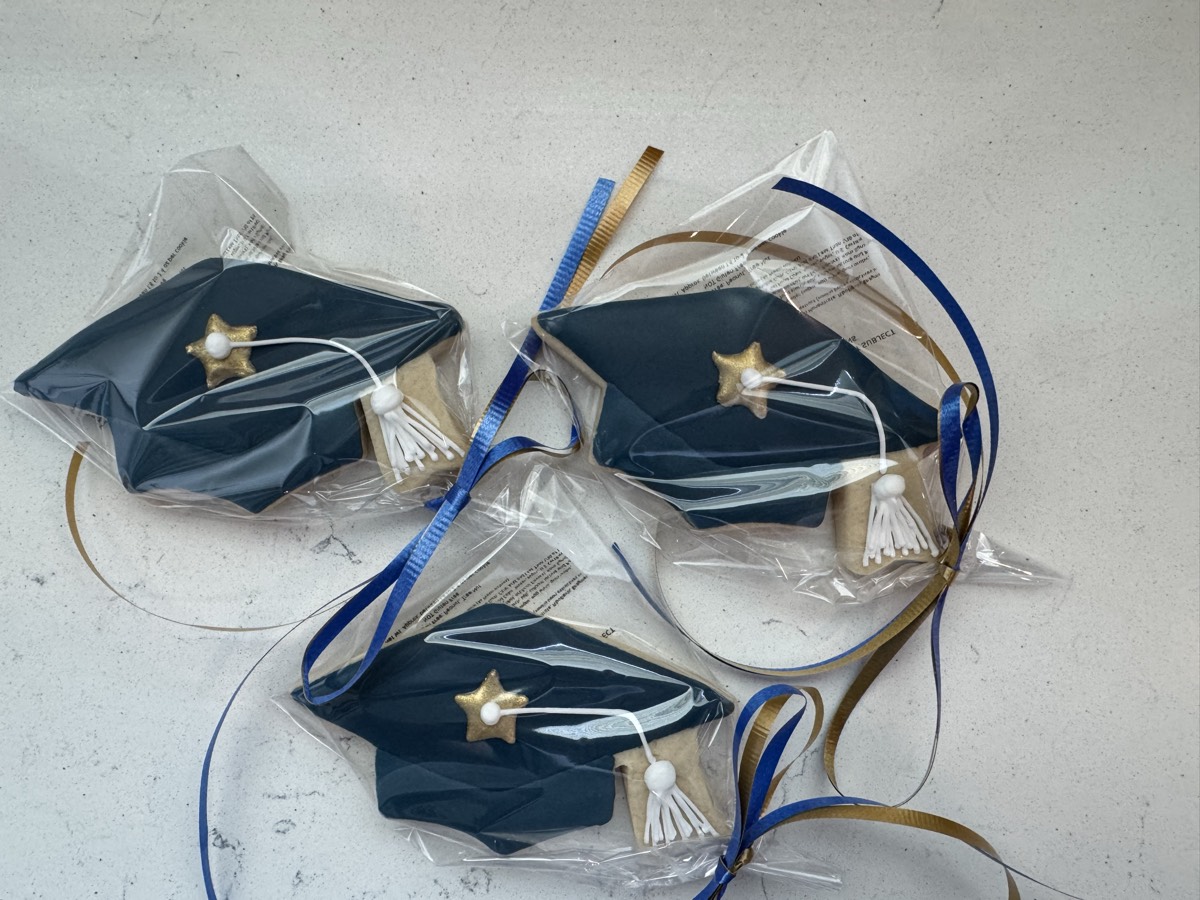 Individually wrapped navy graduation cap cookie favors tied with ribbon, each with a gold star and tassel