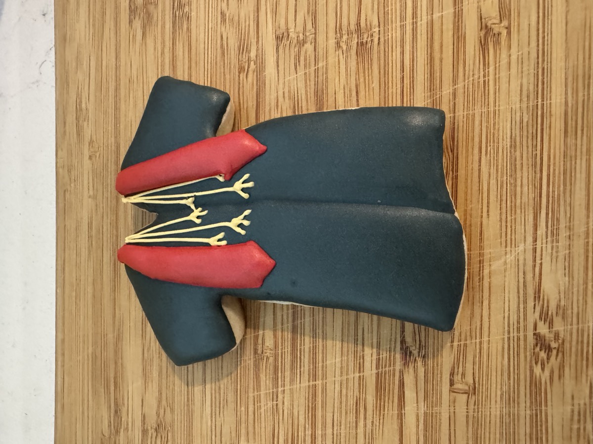 A dark graduation gown decorated sugar cookie with a red honor stole