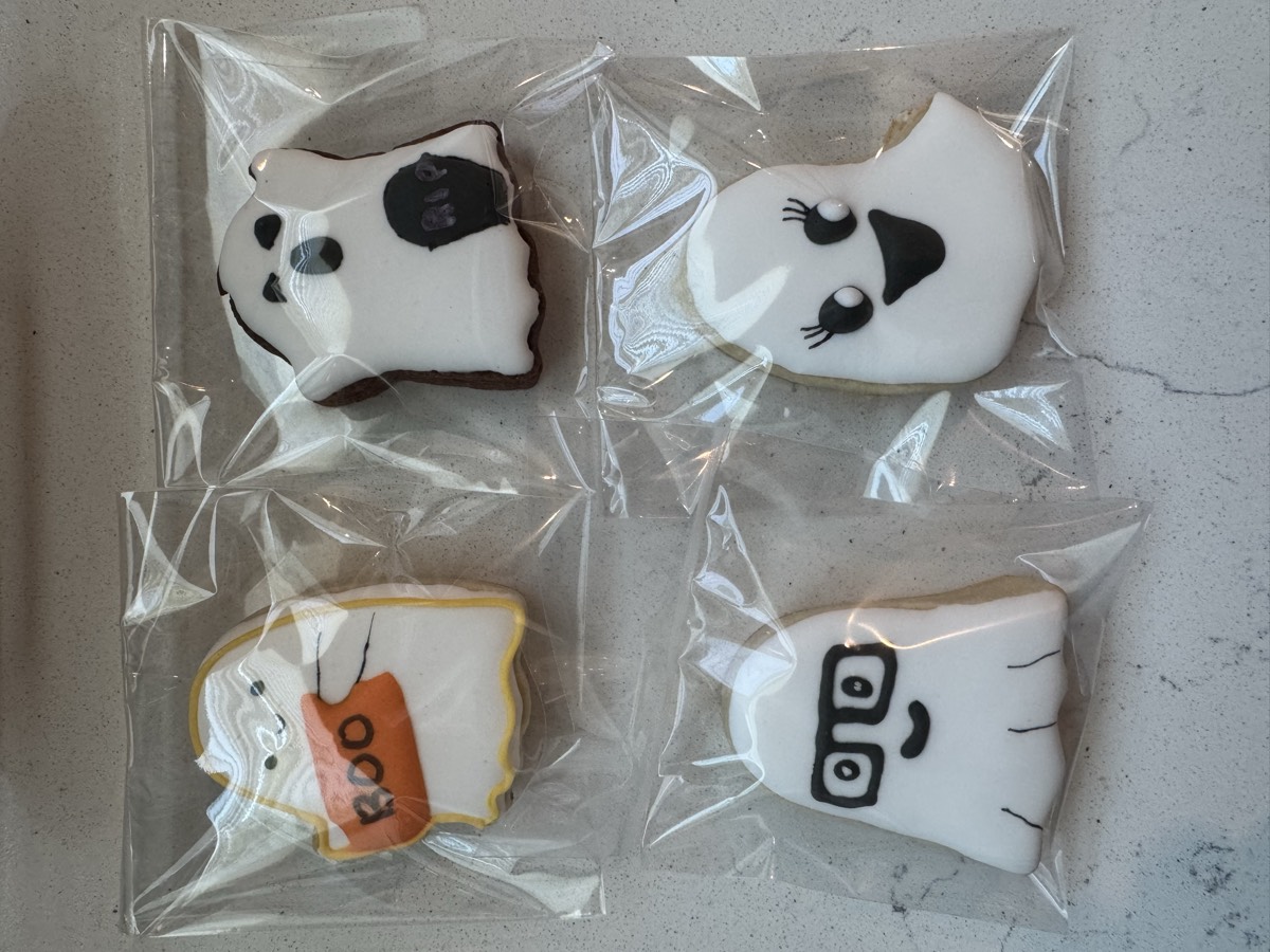 Individually wrapped ghost decorated sugar cookies, one holding a "Boo" sign, one winking, one wearing glasses, and one smiling with lashes