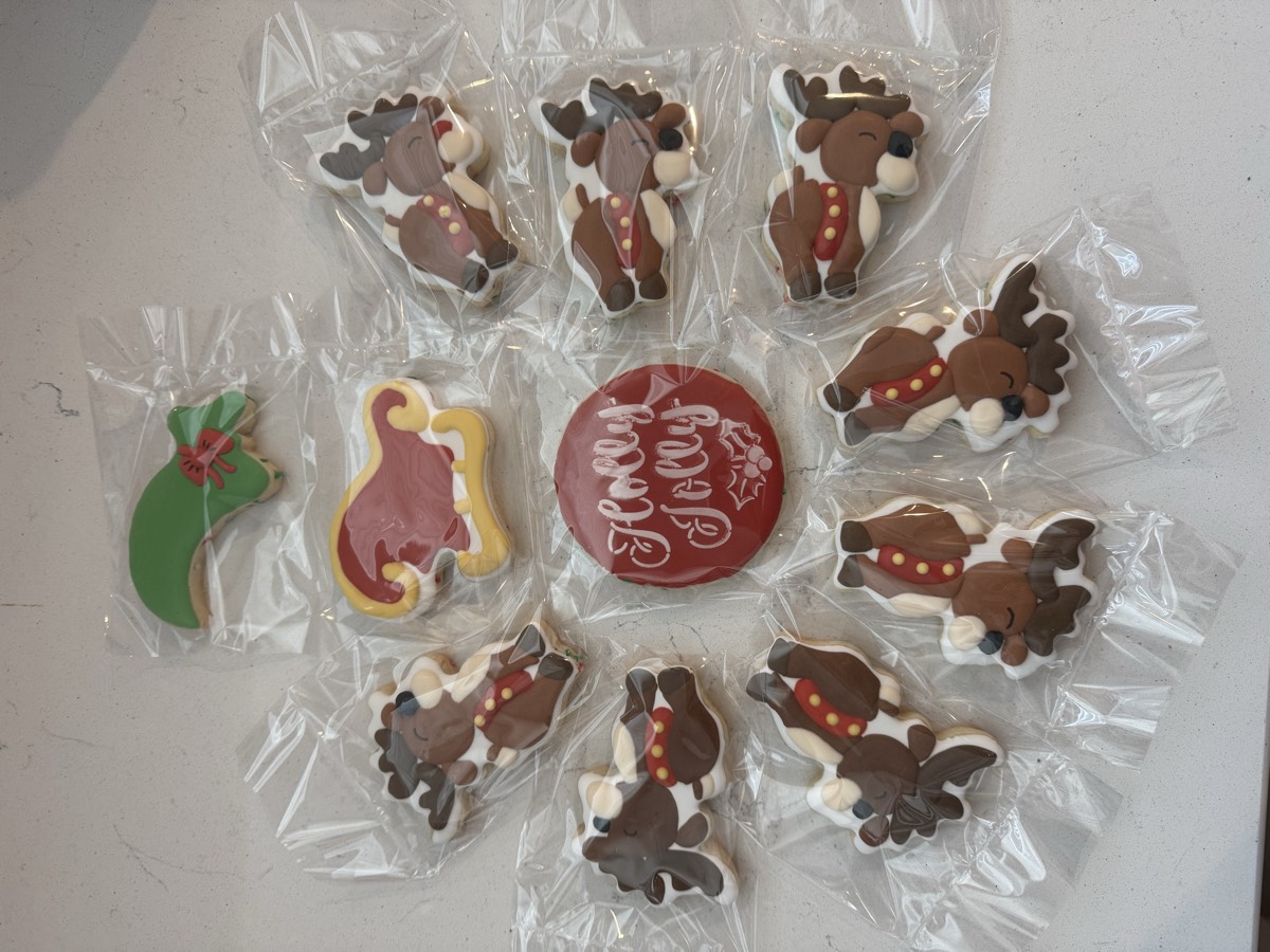 Individually wrapped brown reindeer decorated sugar cookies arranged around a red "Holly Jolly" cookie, with a Santa sleigh and a mistletoe cookie