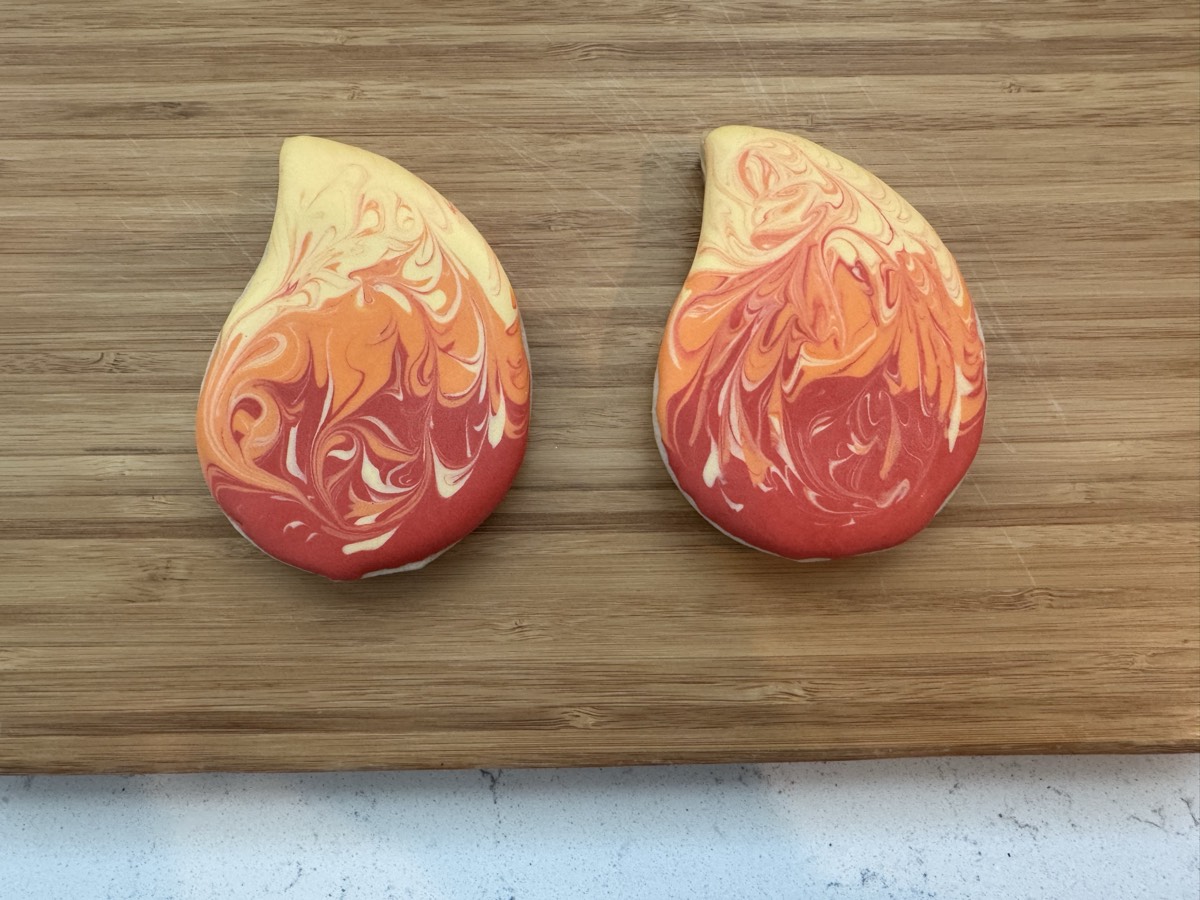 Two teardrop-shaped decorated sugar cookies with a marbled red, orange, and yellow swirl pattern