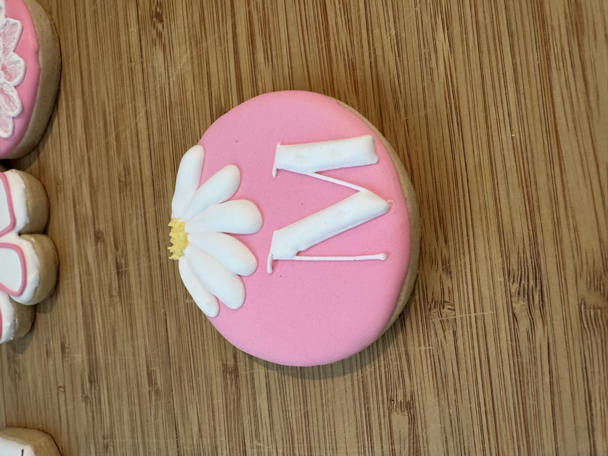 A pink round decorated sugar cookie with a white daisy and a monogram letter