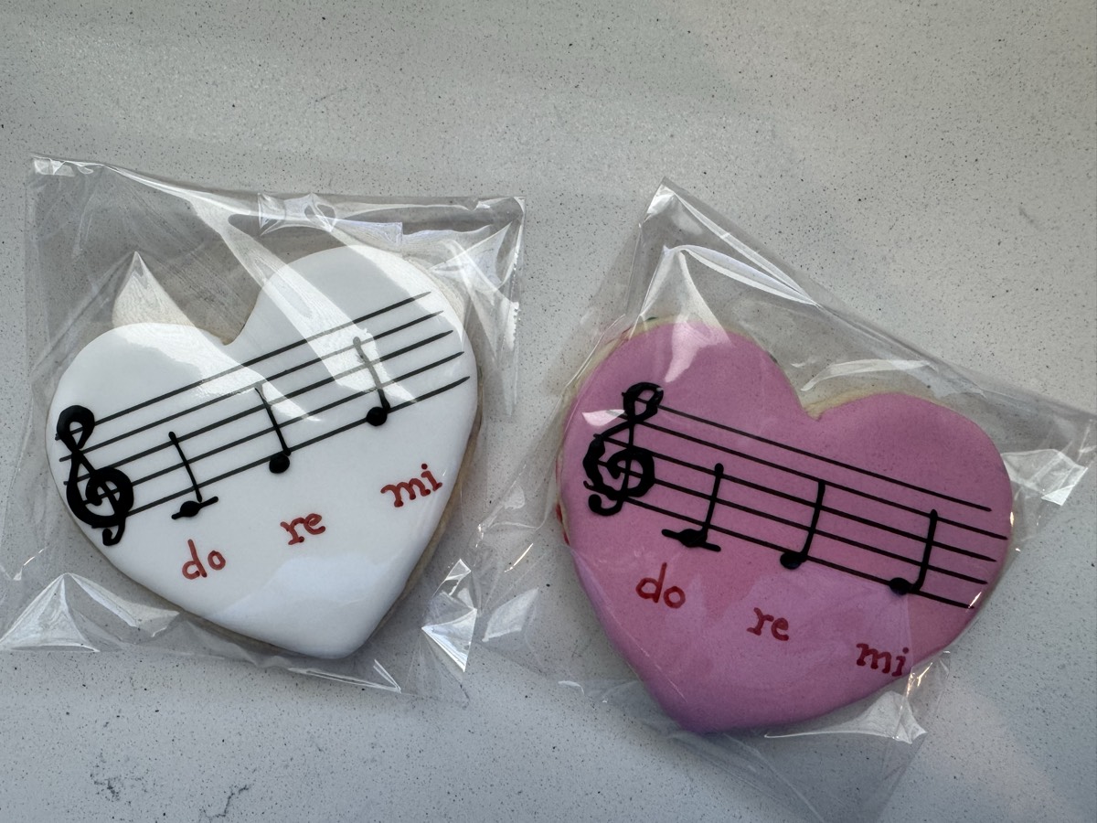 Heart-shaped decorated sugar cookies, one white and one pink, each with a musical staff, treble clef, and "do re mi" lettering