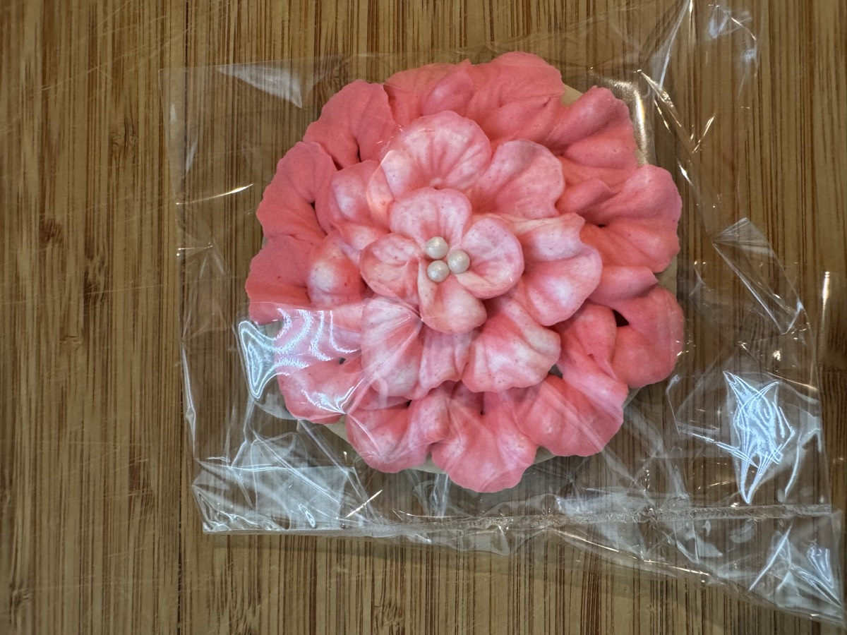 A large pink ruffled flower decorated sugar cookie with a pearl center
