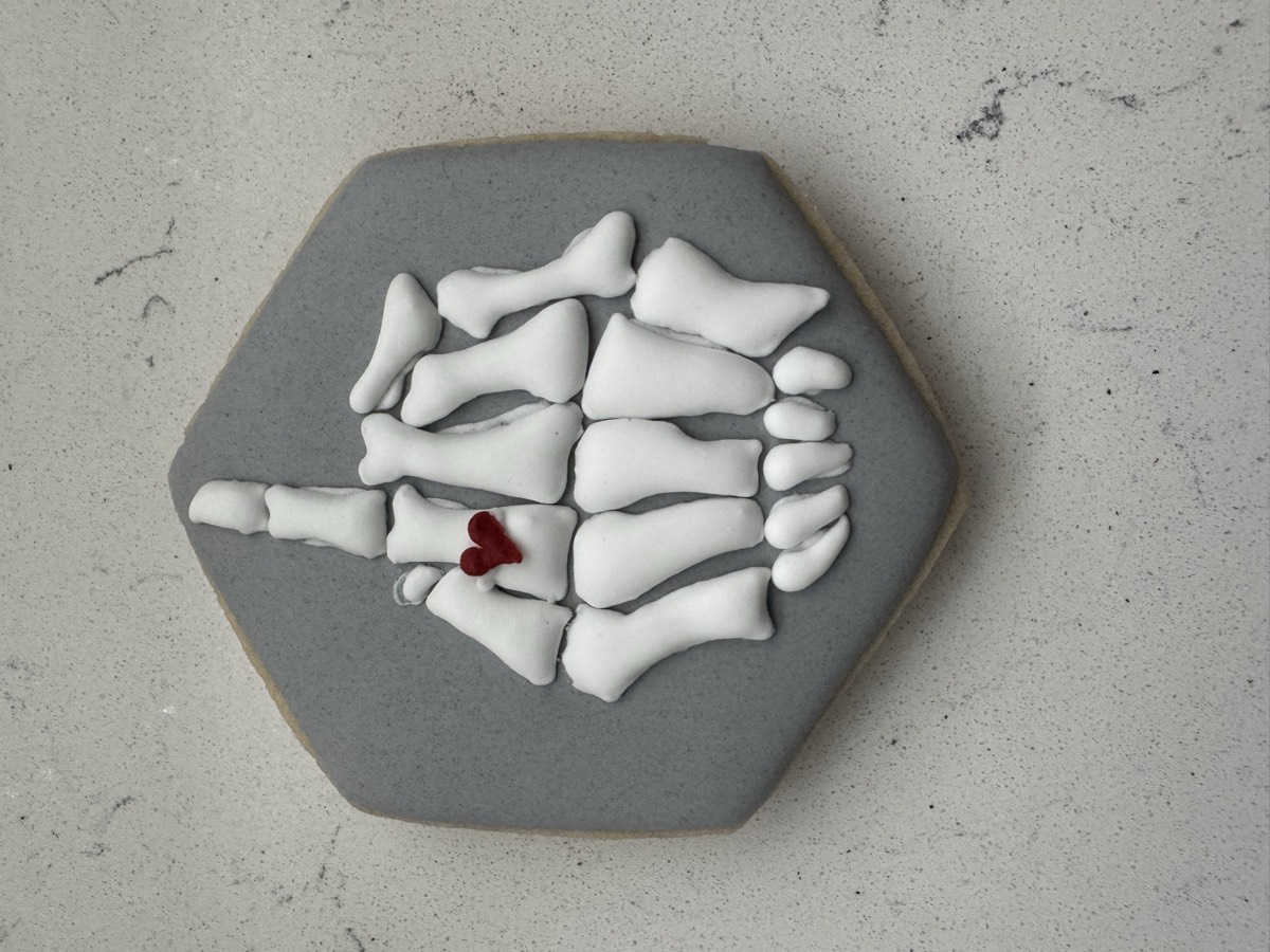 A skeleton hand decorated sugar cookie with a small red heart, iced in white and gray fondant