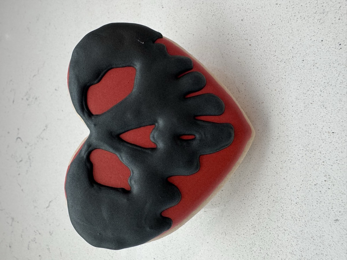 A red heart-shaped decorated sugar cookie with a dripping black skull design
