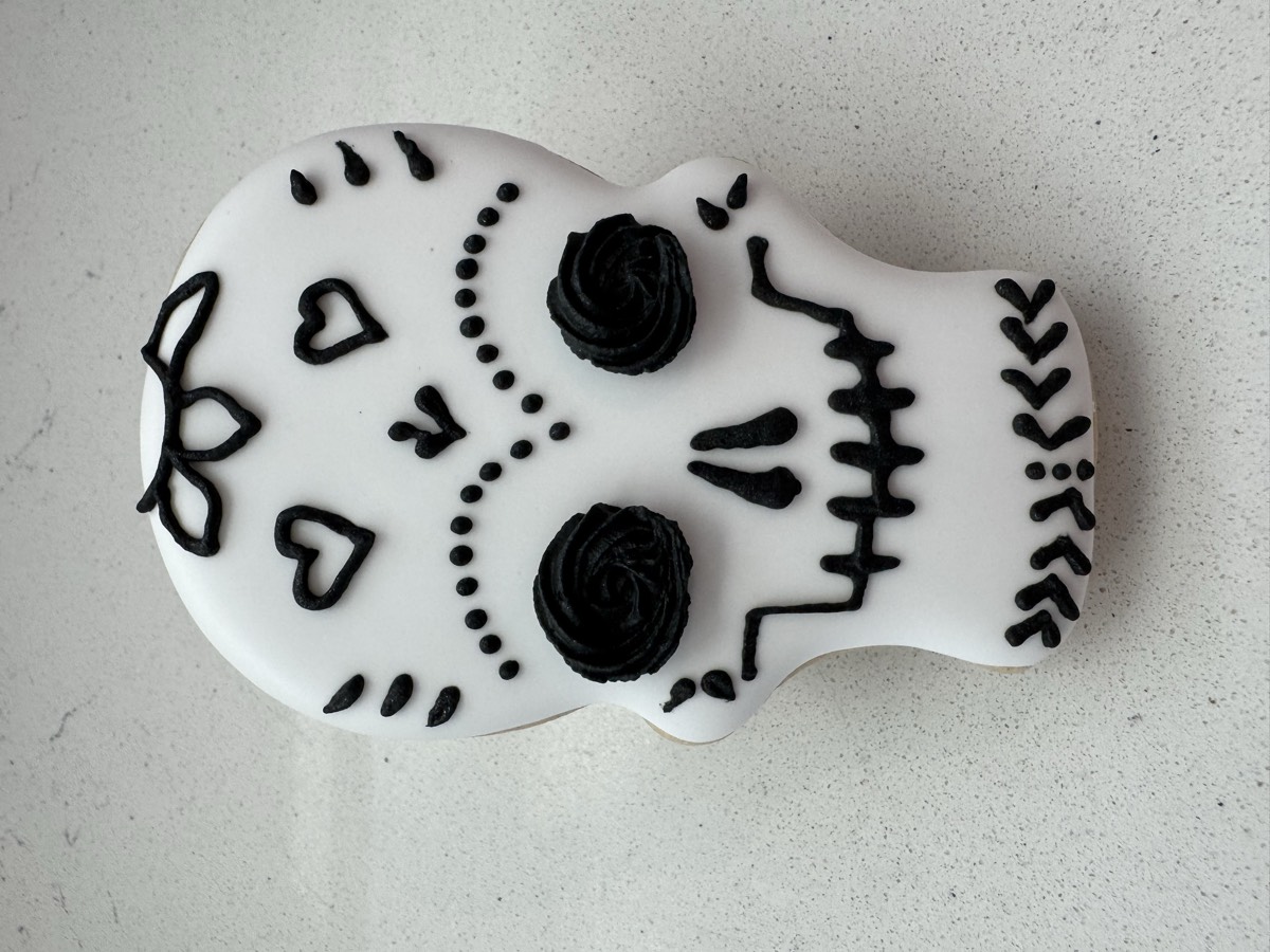 A white Day of the Dead sugar skull decorated sugar cookie with black floral and heart details