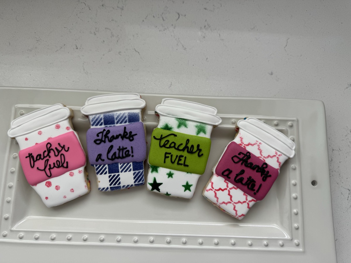 Coffee cup decorated sugar cookies reading "Teacher Fuel" and "Thanks a Latte!" in pink, plaid, purple, and green patterns
