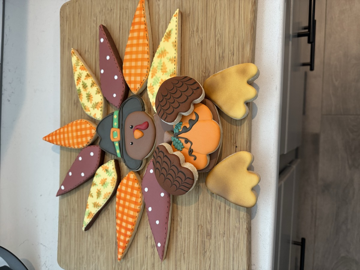 An elaborate Thanksgiving turkey made of decorated sugar cookie feathers in fall patterns, with a pilgrim hat, acorn wings, and turkey feet