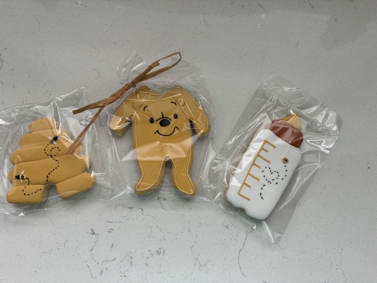 Winnie the Pooh baby shower decorated sugar cookies including a honeybee paw print, a Pooh Bear face, and a honey bottle